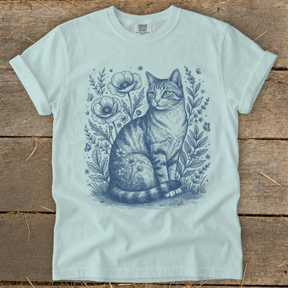Light blue t-shirt with a detailed blue line drawing of a tabby cat among flowers and butterflies.