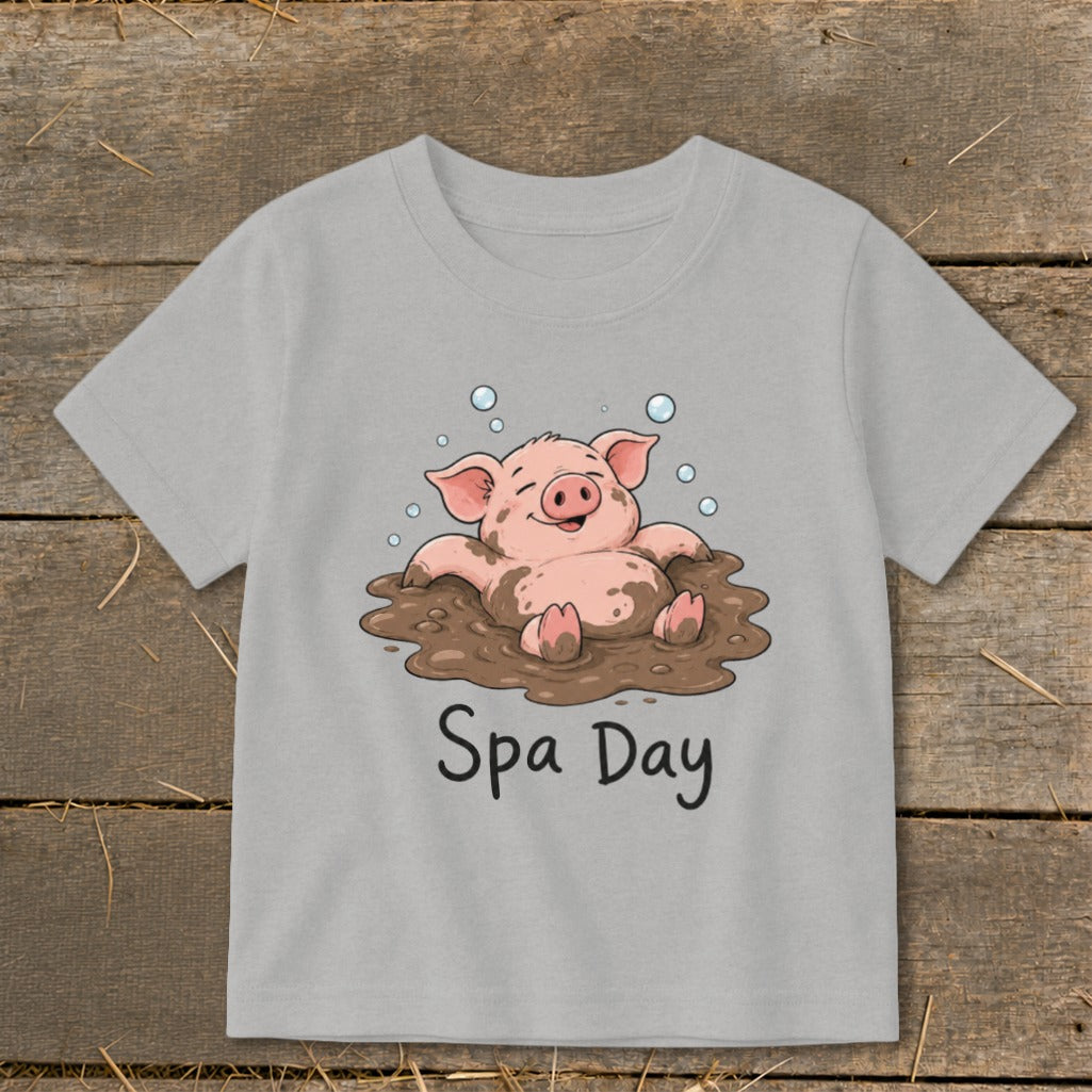 Cartoon pig enjoying a mud bath with "Spa Day" text on a gray t-shirt.