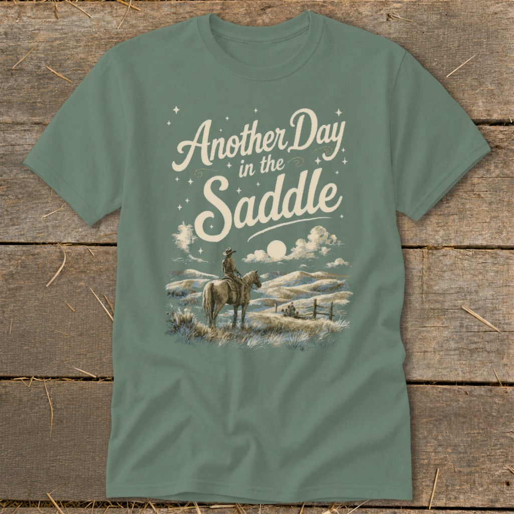 T-shirt graphic: cowboy on horse, moonlit sky, text "Another Day in the Saddle".