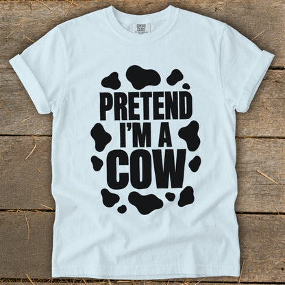 White t-shirt with black "PRETEND I'M A COW" text and cow spots.