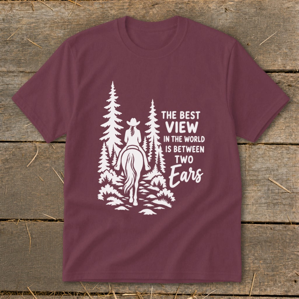 Maroon short-sleeved t-shirt featuring a white graphic of a horseback rider in the woods and text that reads "The best view in the world is between two ears".