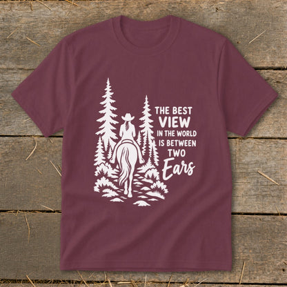 Maroon short-sleeved t-shirt featuring a white graphic of a horseback rider in the woods and text that reads "The best view in the world is between two ears".