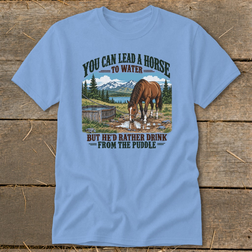 Light blue t-shirt featuring a graphic of a horse drinking from a puddle with mountains and the text You can lead a horse to water but he'd rather drink from the puddle.