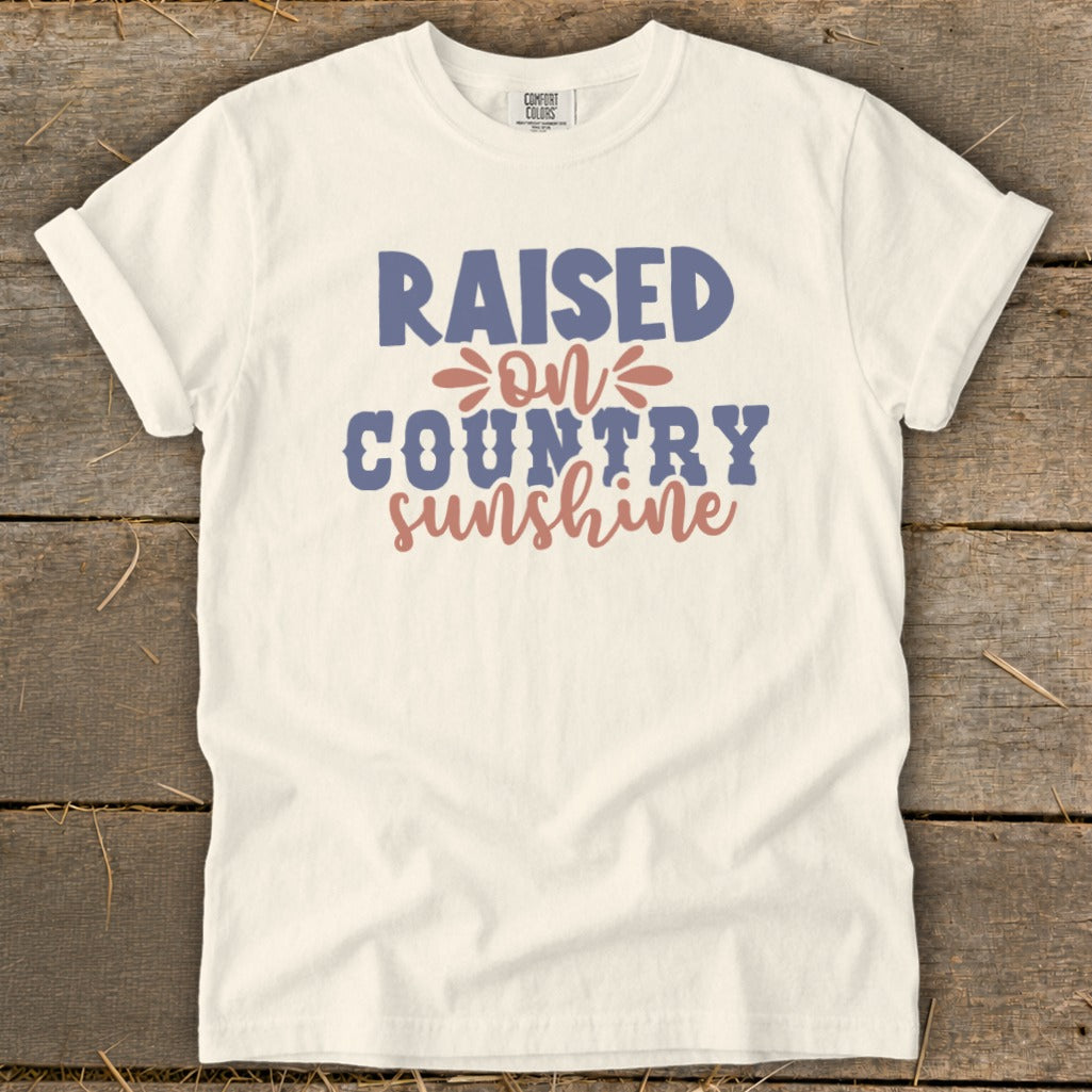 Cream t-shirt with "Raised on Country Sunshine" text in blue and coral.