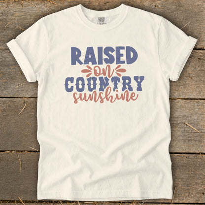 Cream t-shirt with "Raised on Country Sunshine" text in blue and coral.