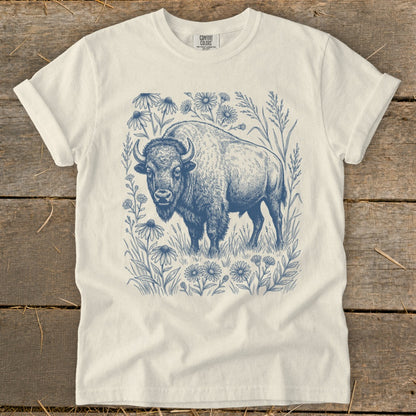 Bison surrounded by flowers and grass in a blue line drawing on a cream t-shirt.