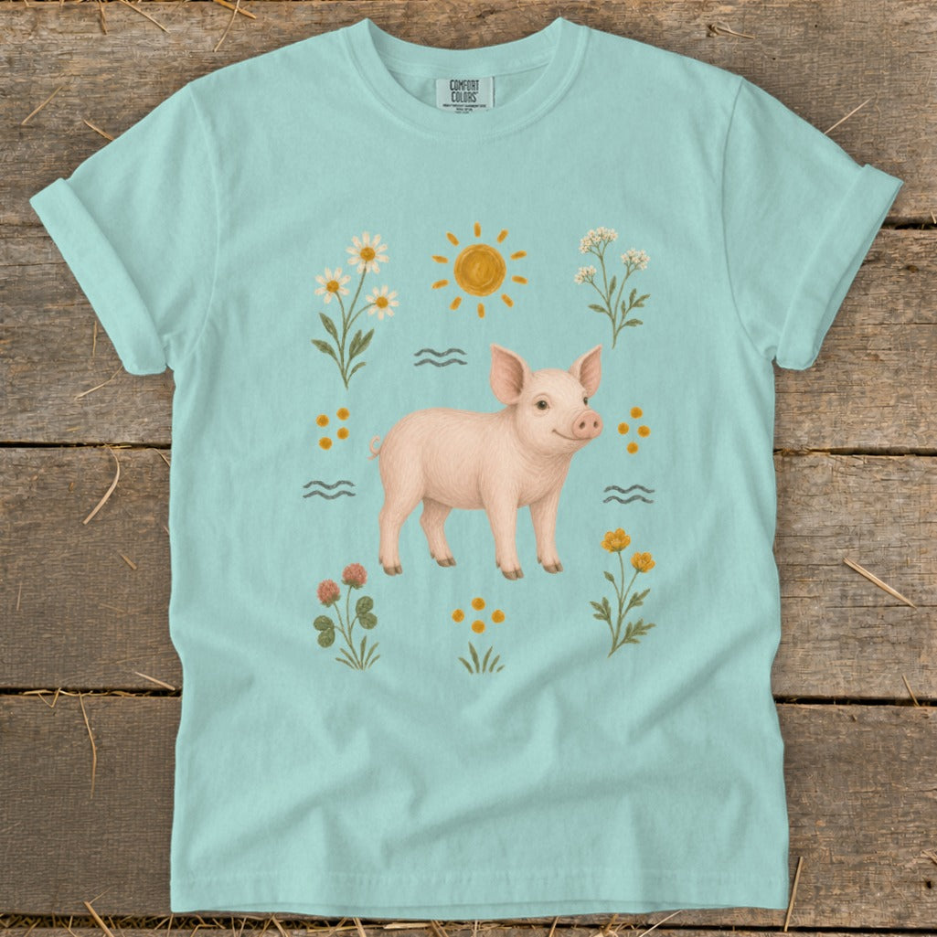 Pale blue t-shirt with a piglet illustration surrounded by flowers and a sun.