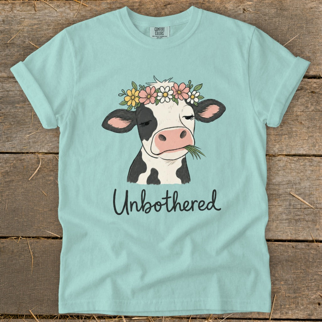 Cow with flower crown eating grass, text "Unbothered".