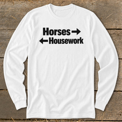 A white long-sleeved t-shirt features black text that reads Horses with a right-pointing arrow above Housework with a left-pointing arrow.
