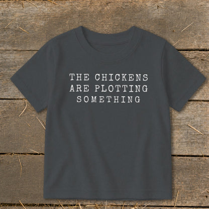 Dark gray t-shirt with white text "THE CHICKENS ARE PLOTTING SOMETHING"