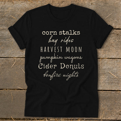 Black t-shirt with white text listing autumn activities like corn stalks, hay rides, and cider donuts.