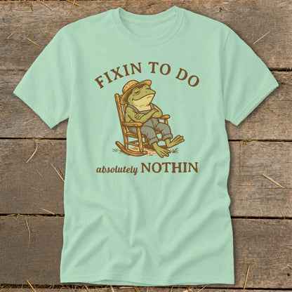 Mint t-shirt with cartoon frog in rocking chair, text "FIXIN TO DO absolutely NOTHIN".