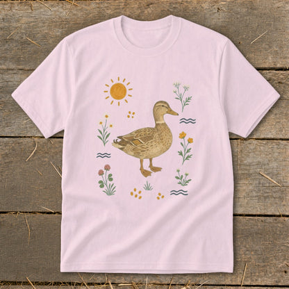 Pink t-shirt with a watercolor illustration of a duck surrounded by flowers and sun.