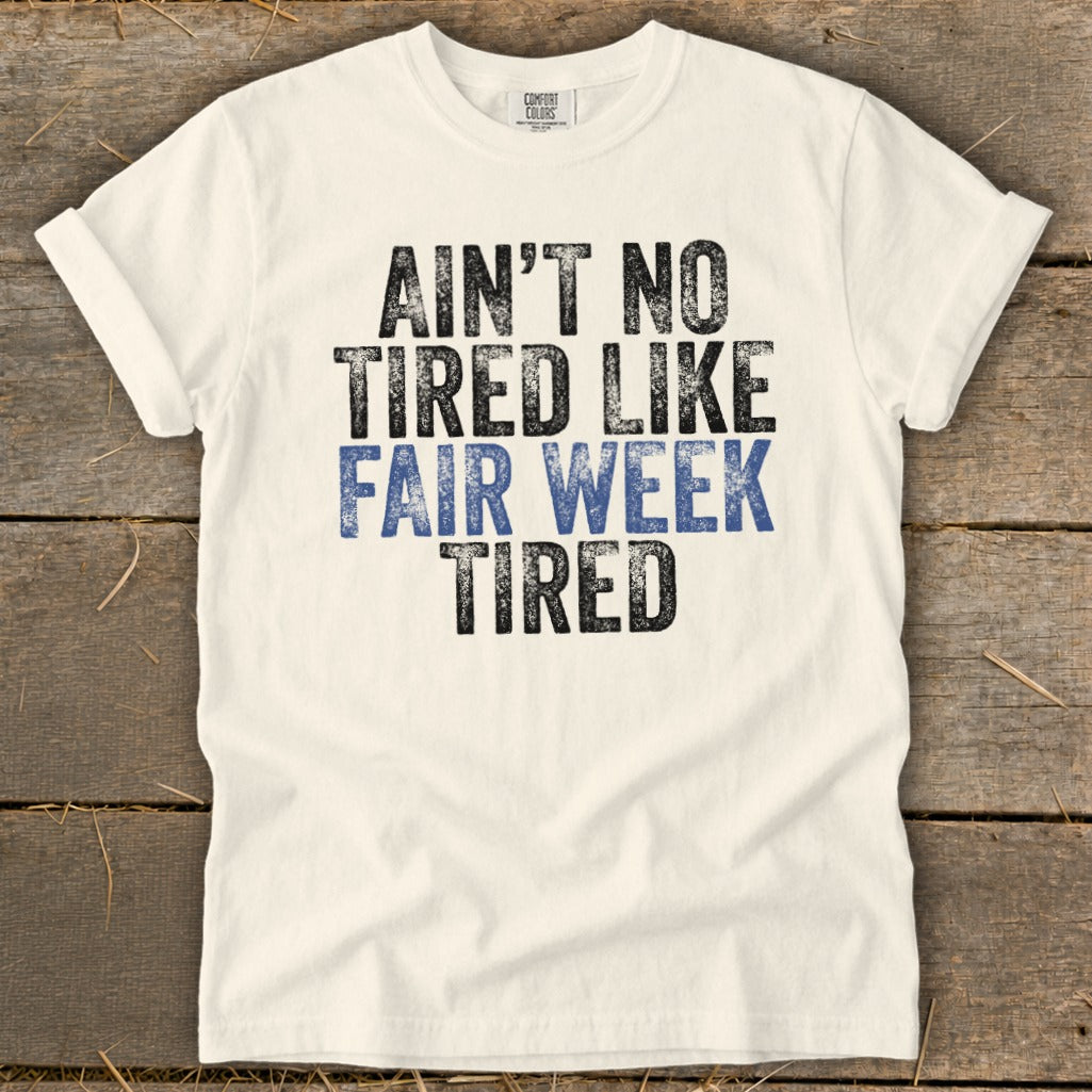 White t-shirt with distressed black and blue text saying "Ain't No Tired Like Fair Week Tired."