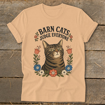Tabby cat with stern expression surrounded by flowers, text reads "Barn Cats Judge Everyone."