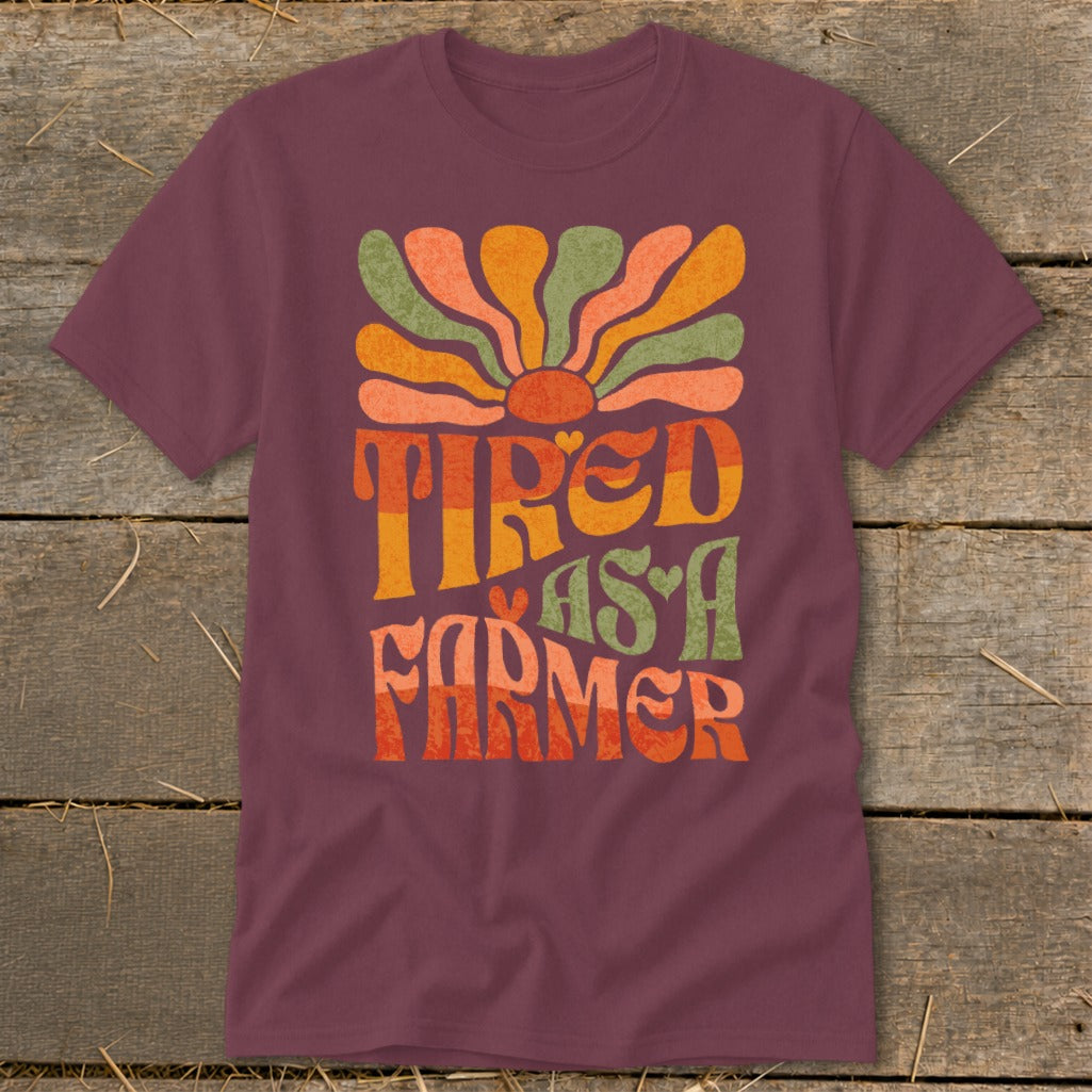 Maroon t-shirt with colorful "Tired as a Farmer" text and sun graphic.