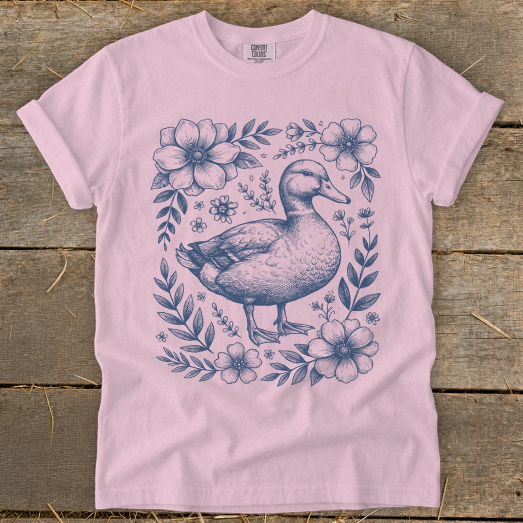 Pink t-shirt with a blue ink drawing of a duck surrounded by flowers and leaves.