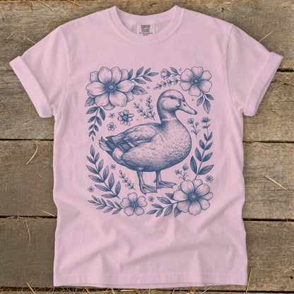 Pink t-shirt with a blue ink drawing of a duck surrounded by flowers and leaves.