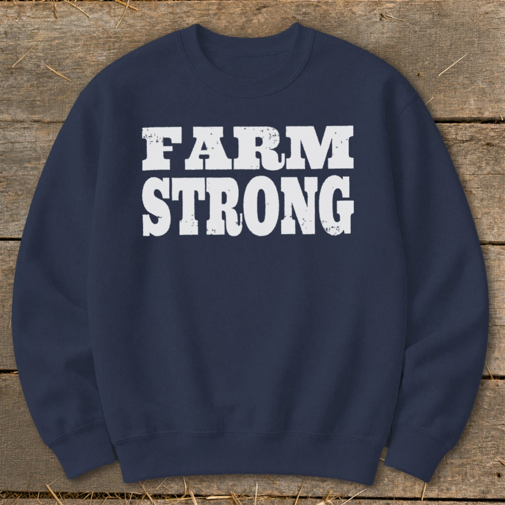 Dark blue crewneck sweatshirt featuring white distressed text that reads FARM STRONG on a wooden background.