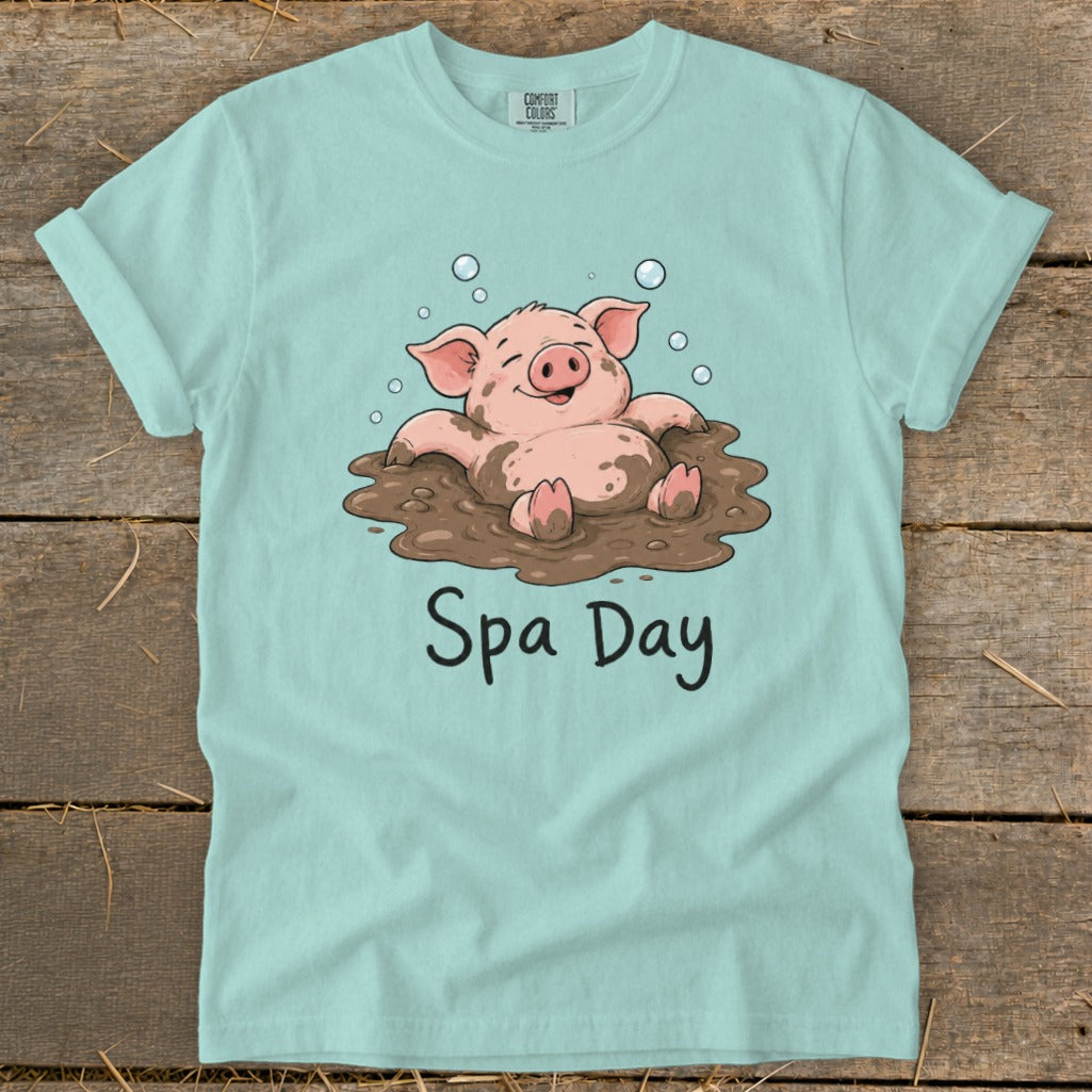 Light blue t-shirt featuring a happy pig covered in mud and bubbles with the words "Spa Day".