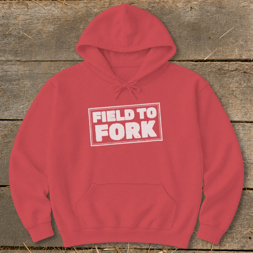 A red hooded sweatshirt with a white outlined rectangular box containing the distressed white text FIELD TO FORK.