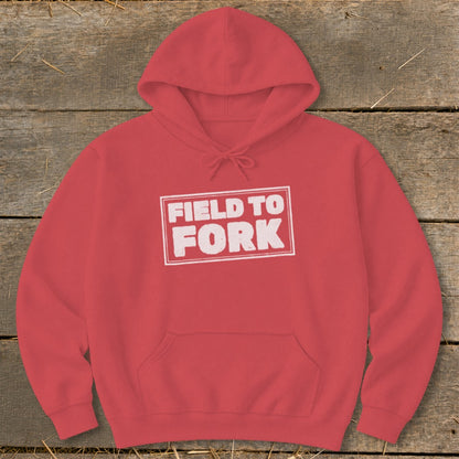 A red hooded sweatshirt with a white outlined rectangular box containing the distressed white text FIELD TO FORK.
