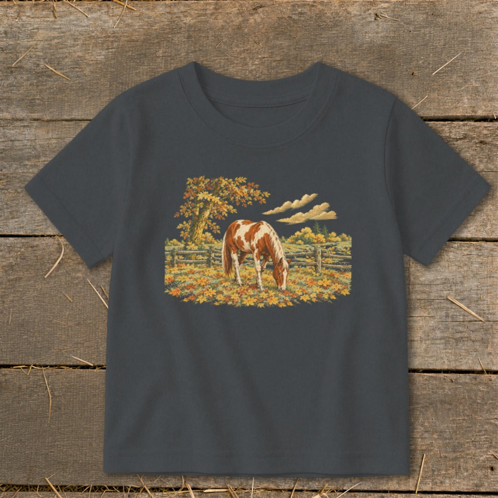 Brown and white horse grazing in a field of autumn leaves.
