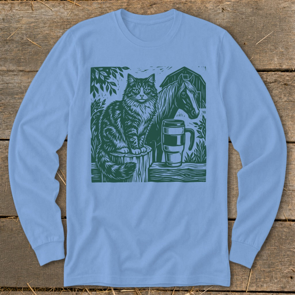 Green linocut print on light blue long-sleeve shirt depicts cat, horse, mug, and barn.