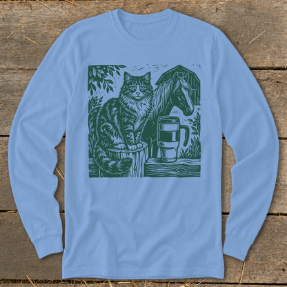 Green linocut print on light blue long-sleeve shirt depicts cat, horse, mug, and barn.