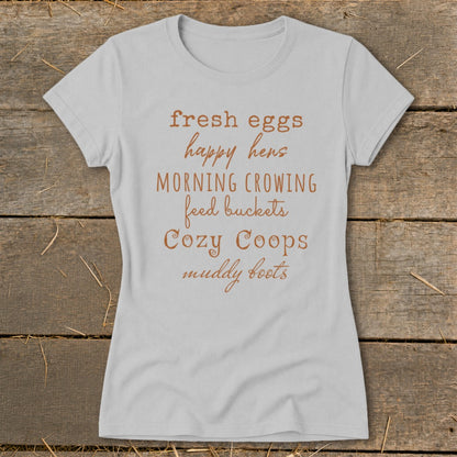 Light grey t-shirt with text: fresh eggs, happy hens, morning crowing, feed buckets, cozy coops, muddy boots.