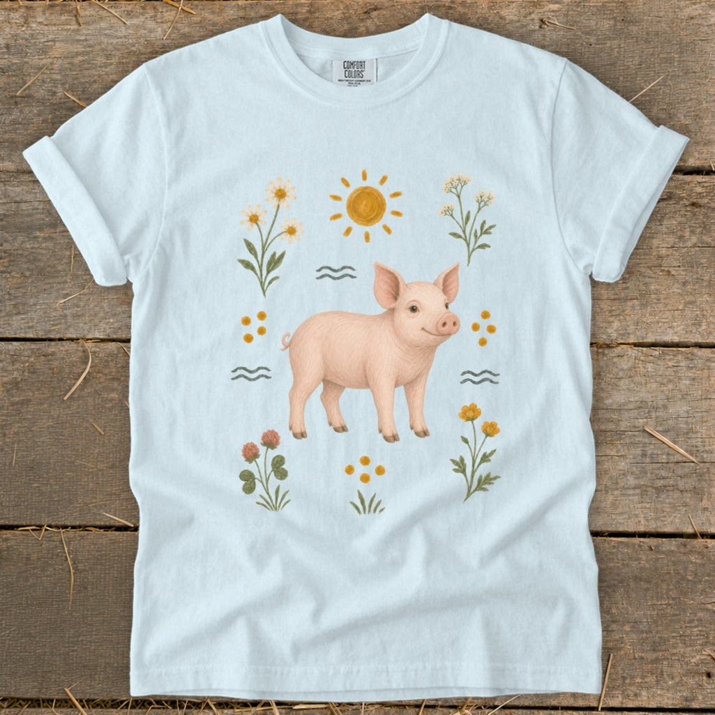 Light blue t-shirt with a pink piglet surrounded by flowers and sun graphic.