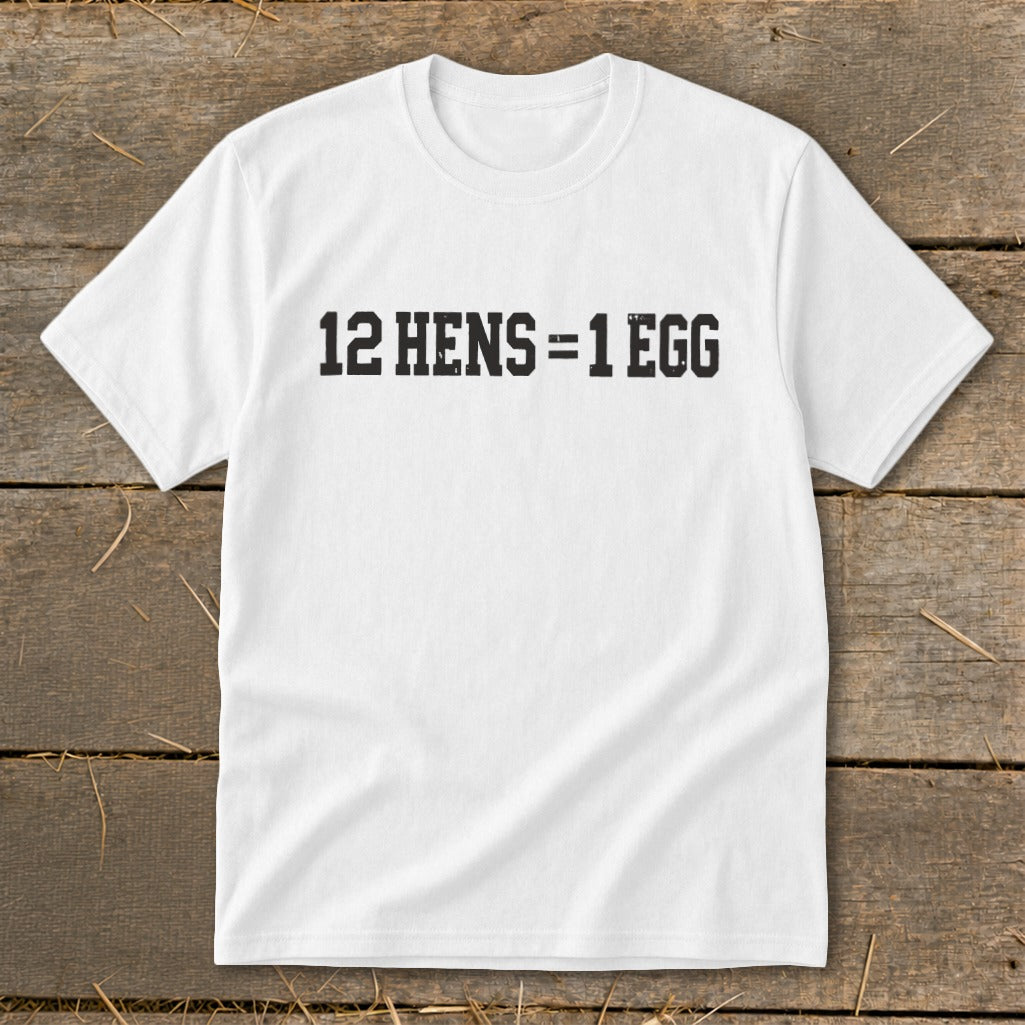 A white t-shirt featuring the black distressed text 12 HENS = 1 EGG on a rustic wooden background.