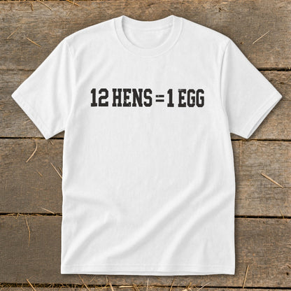 A white t-shirt featuring the black distressed text 12 HENS = 1 EGG on a rustic wooden background.