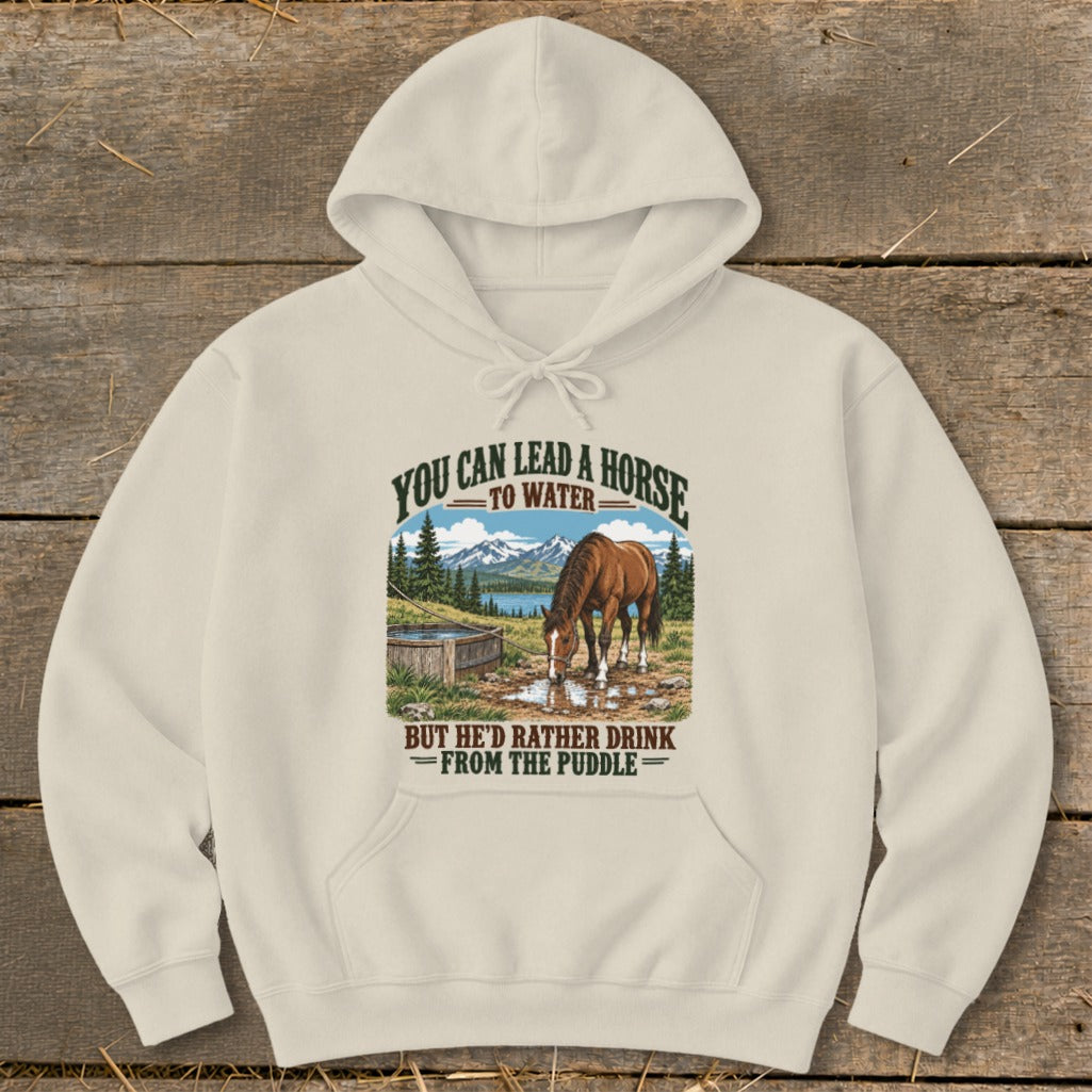 A cream-colored pullover hoodie featuring a graphic of a horse drinking from a puddle with text above and below.