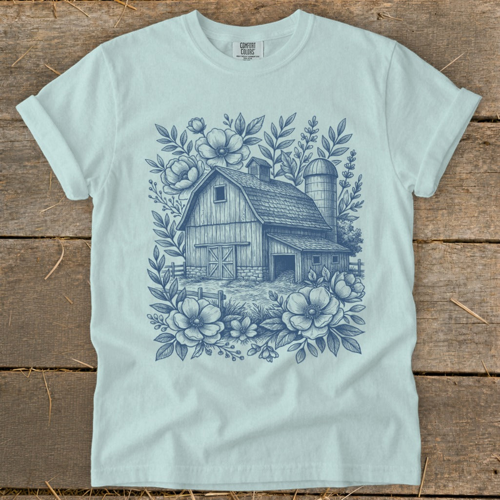Light blue t-shirt with a blue sketch of a barn and silo surrounded by flowers.