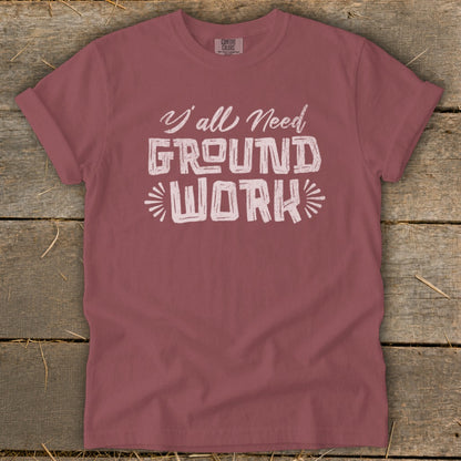 Rose-colored t-shirt with "Y'all Need GROUND WORK" graphic.