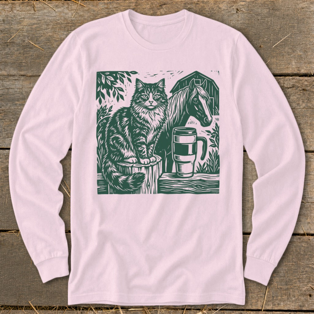 Green linocut of a cat, horse, barn, and mug on a pink long-sleeve shirt.