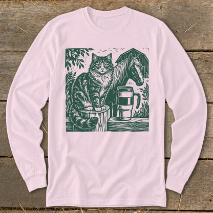 Green linocut of a cat, horse, barn, and mug on a pink long-sleeve shirt.