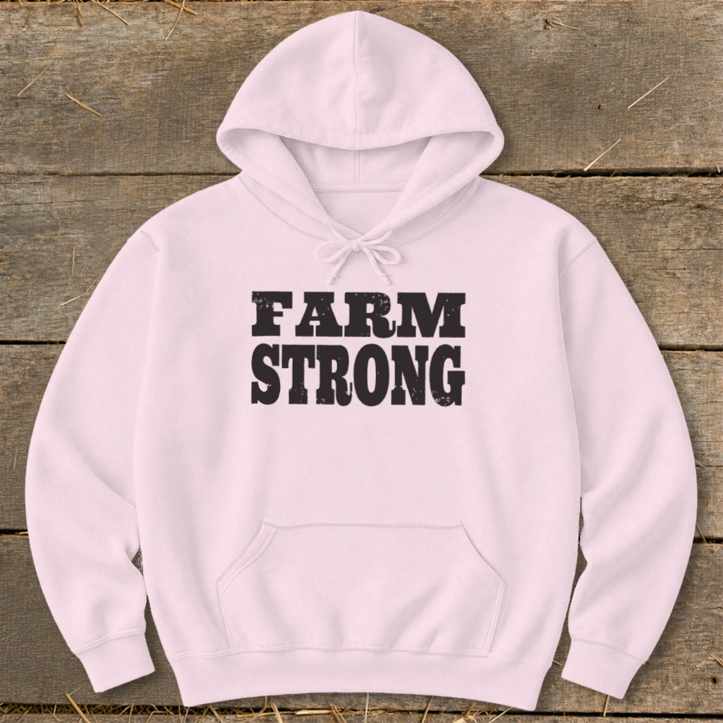 Light pink hooded sweatshirt with black distressed text reading FARM STRONG centered on a rustic wooden background.