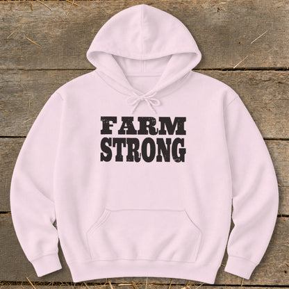 Light pink hooded sweatshirt with black distressed text reading FARM STRONG centered on a rustic wooden background.