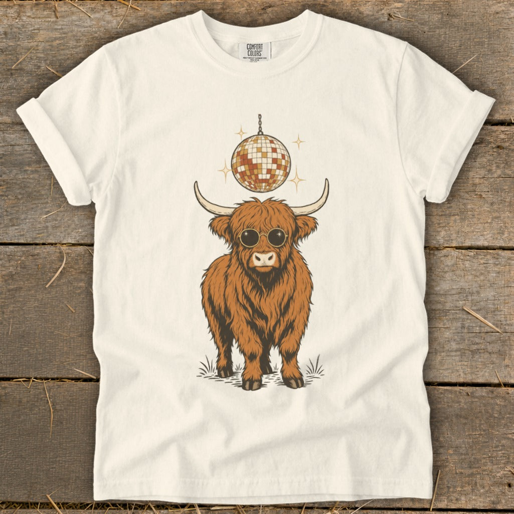 Highland cow with sunglasses and disco ball graphic on a cream t-shirt.