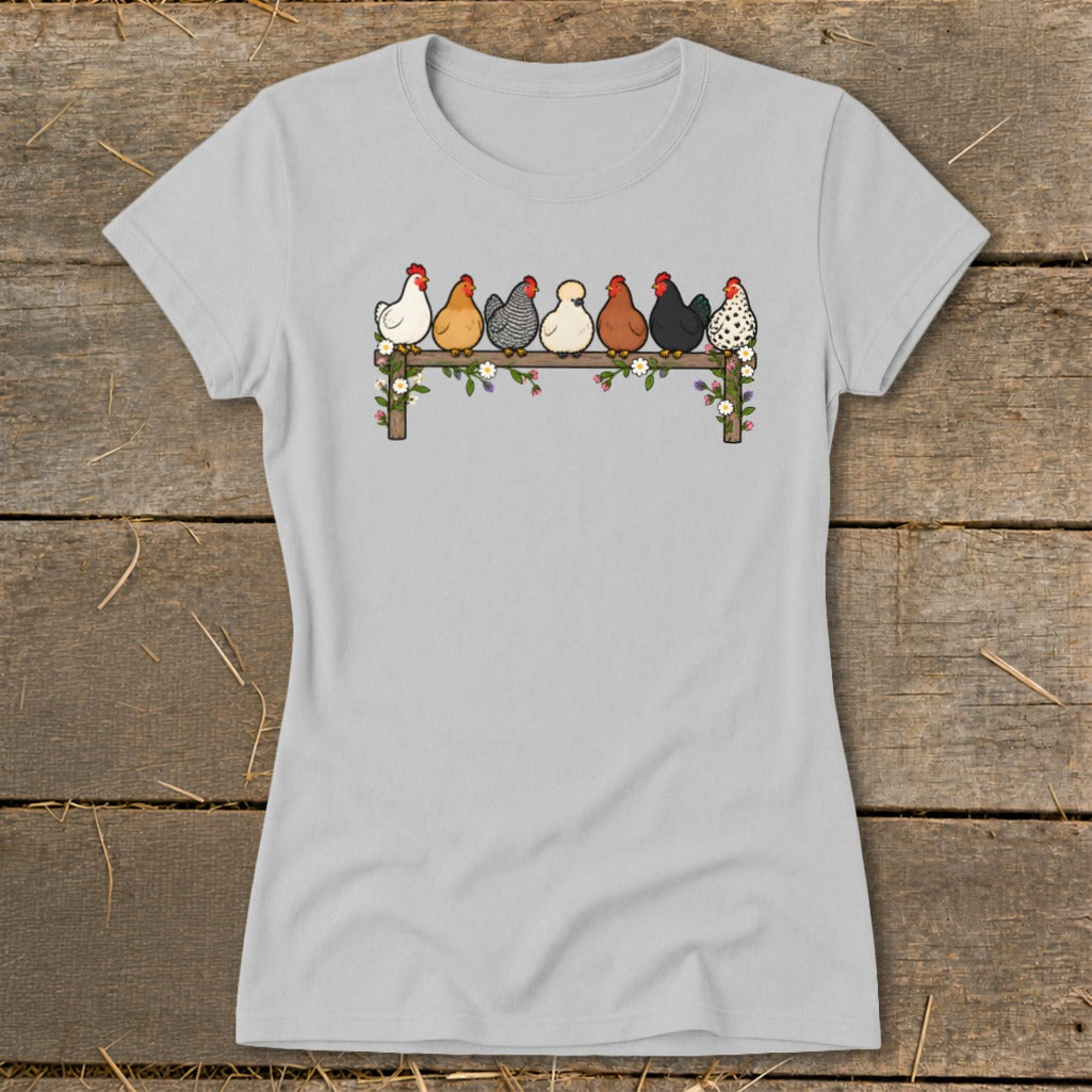 A light gray women's t-shirt features a colorful illustration of seven diverse chickens perched on a flower-decorated fence.