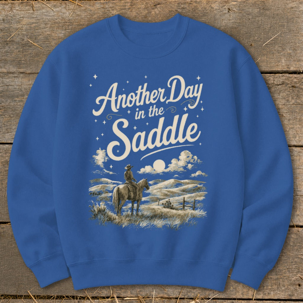Blue sweatshirt with "Another Day in the Saddle" text and cowboy on horseback graphic.