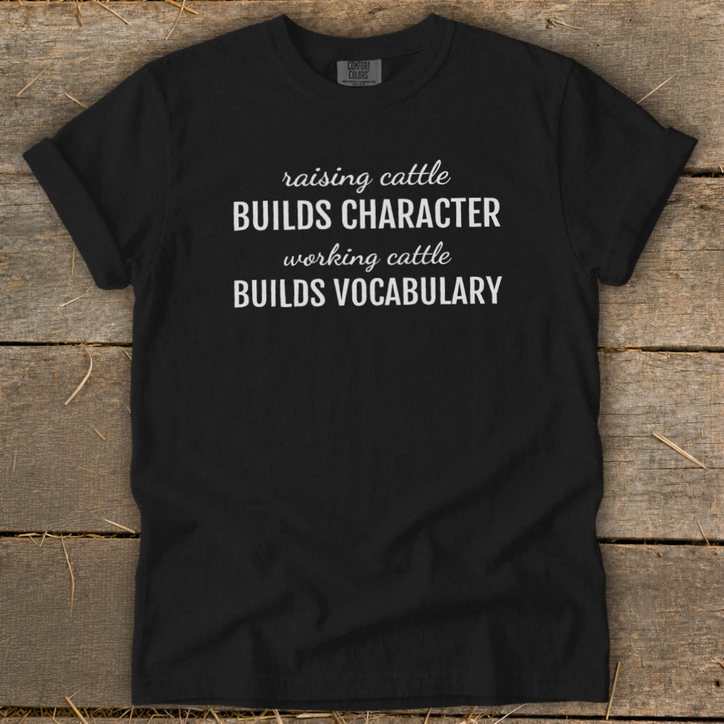 Black t-shirt with white text: "raising cattle BUILDS CHARACTER, working cattle BUILDS VOCABULARY."