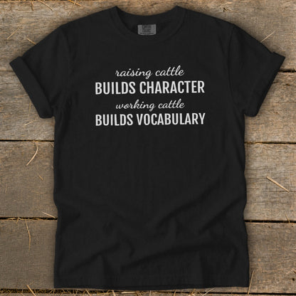Black t-shirt with white text: "raising cattle BUILDS CHARACTER, working cattle BUILDS VOCABULARY."