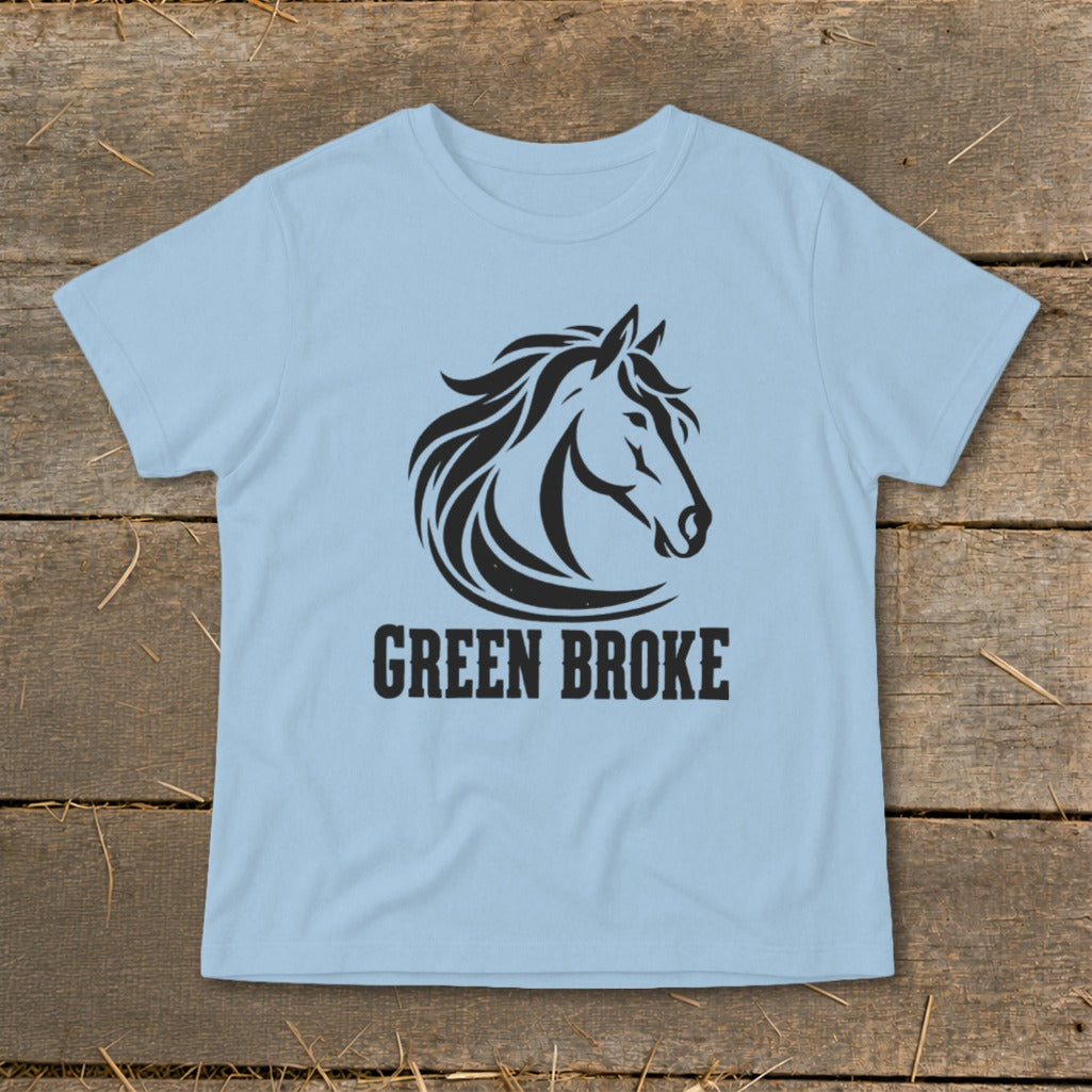 Light blue crewneck t-shirt featuring a black graphic of a horse head and the text GREEN BROKE, laid flat on rustic wood.