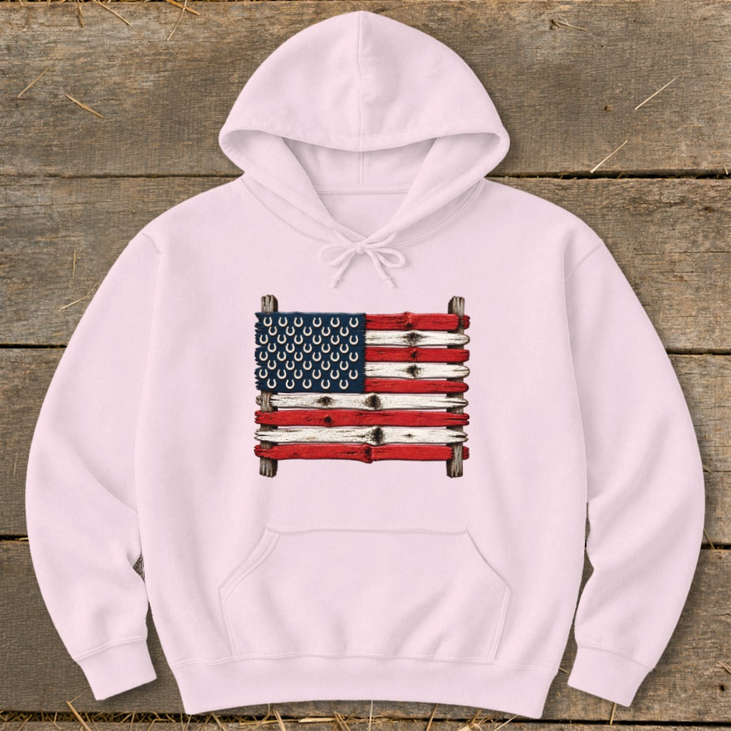 A light pink pullover hoodie features an American flag graphic made of painted wooden planks and horseshoes.