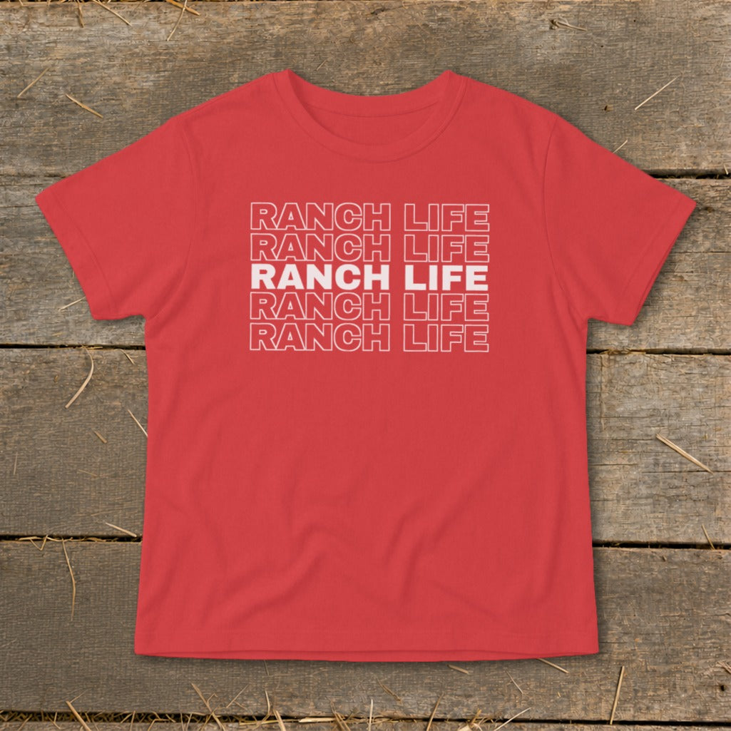 A red t-shirt with the stacked white text "RANCH LIFE" on a wooden background.