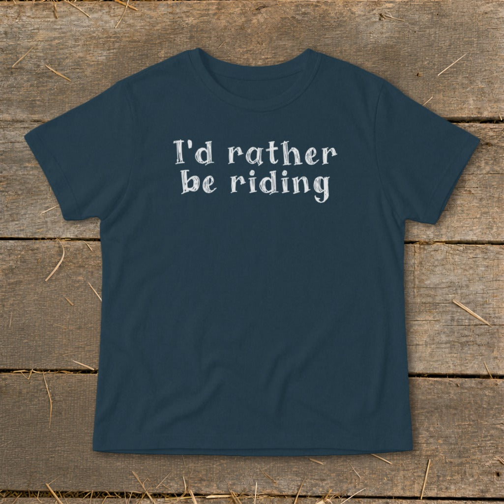 Dark blue t-shirt with white text "I'd rather be riding" on a wooden background.