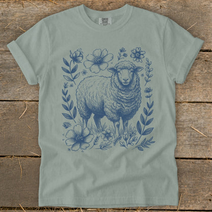 Blue sheep illustration with floral border on a light green t-shirt.